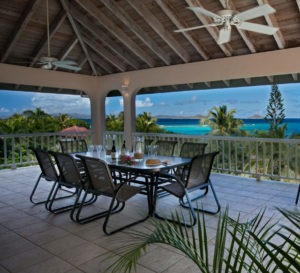 A serene outdoor dining terrace featuring a round table set for six, overlooking a stunning ocean view at sunset.