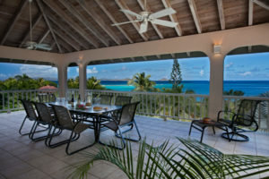 Covered outdoor dining patio at Adagio Villa in Virgin Gorda with panoramic ocean views, featuring a dining table for six, comfortable seating, and lush tropical vegetation framing the turquoise Caribbean waters of Mahoe Bay
