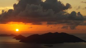 Sunset with vibrant orange and red hues, silhouetted islands, and dramatic clouds at Adagio Villa Resort.