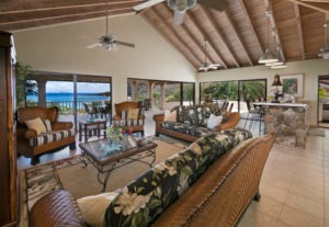 A spacious living room featuring comfortable wicker furniture, large windows offering ocean views, and a stone bar area.