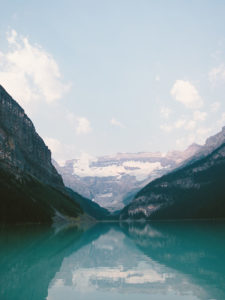 A serene lake with crystal-clear turquoise waters, reflecting the majestic snow-capped mountains under a bright blue sky.