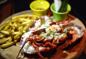 Grilled lobster served on a wooden board with a side of fries and dipping sauces at Adagio Villa Resort.