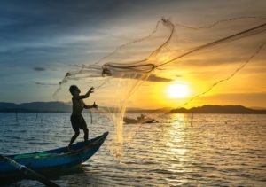 Fisherman on a small boat casting a net into the water during a stunning sunset at Adagio Villa Resort.