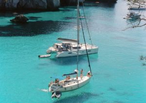 Catamaran and sailing yacht docked in vibrant turquoise waters, surrounded by rocky cliffs at Adagio Villa Resort.