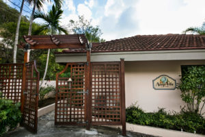 Wooden gate and sign for Adagio Villa Resort, surrounded by lush greenery and tropical plants.