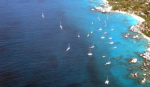 Aerial shot of sailboats scattered across turquoise waters near a rocky shoreline at Adagio Villa Resort.