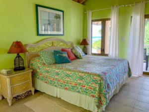 Guest room with bright green walls, a colorful bedspread, and a cozy seating area overlooking the outdoors at Adagio Villa Resort.