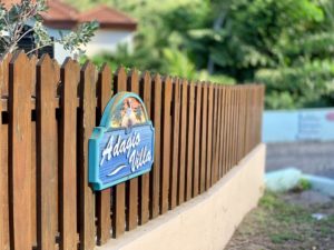 Wooden fence with the Adagio Villa sign, featuring a colorful design and tropical imagery.