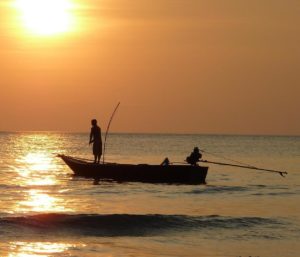 Silhouette of a fisherman standing on a small boat, fishing at sunset with the sun glowing in the background at Adagio Villa Resort.