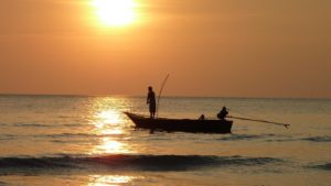 Silhouette of a fisherman standing on a small boat, fishing at sunset with the sun glowing in the background at Adagio Villa Resort.