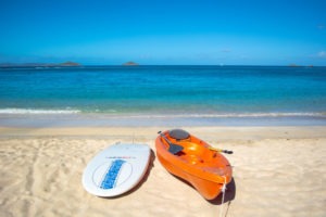 Orange kayak and white surfboard resting on a pristine sandy beach with turquoise waters in the background at Adagio Villa Resort.