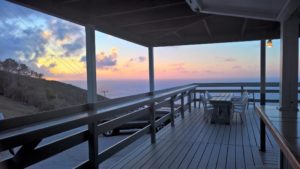 Oceanfront deck with wooden railing and seating, overlooking a stunning sunset at Adagio Villa Resort.