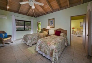 Cozy tropical guest room with two twin beds, a comfortable armchair, and warm lighting.